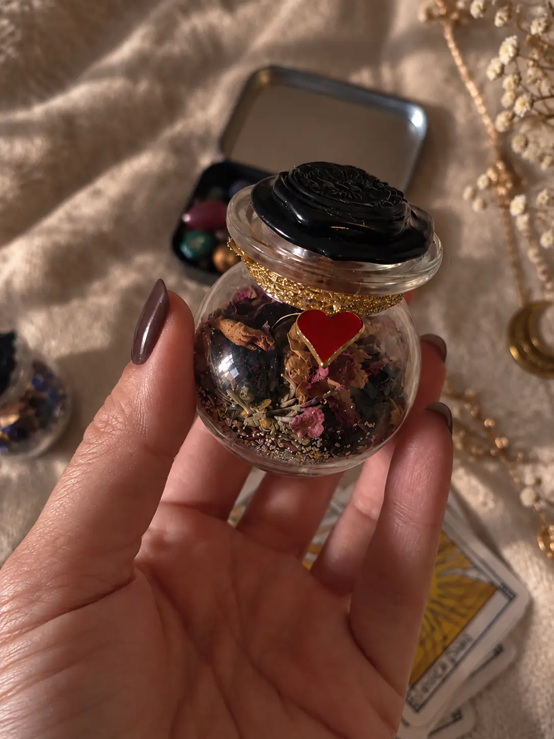 Petite fiole spell jar amour remplie de pétales et d'herbes, breloque cœur rouge, tenue à la main
