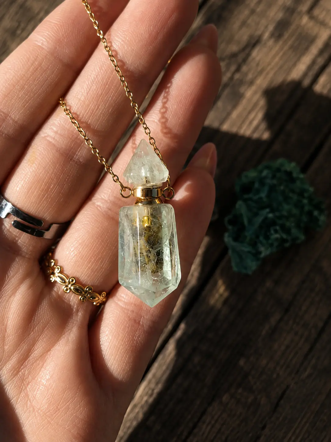 Amulette fiole en aventurine verte et chaîne dorée, tenue dans une main au soleil