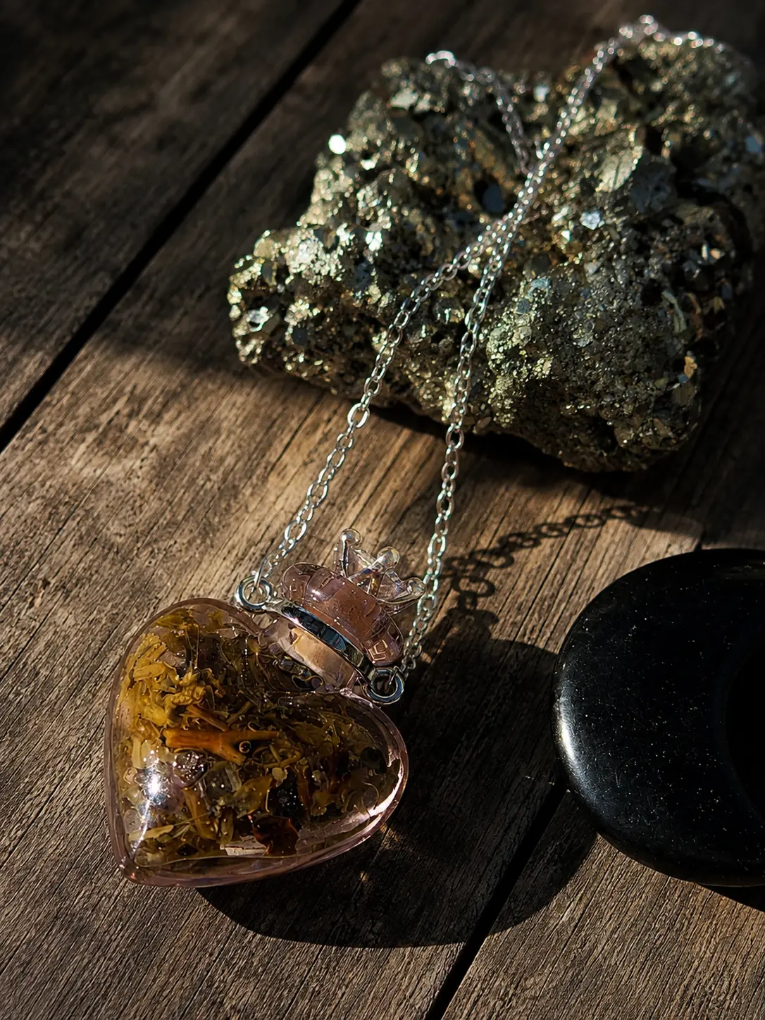 Amulette fiole en forme de cœur remplie d'herbes et de cristaux, chaîne argentée, sur un bois patiné