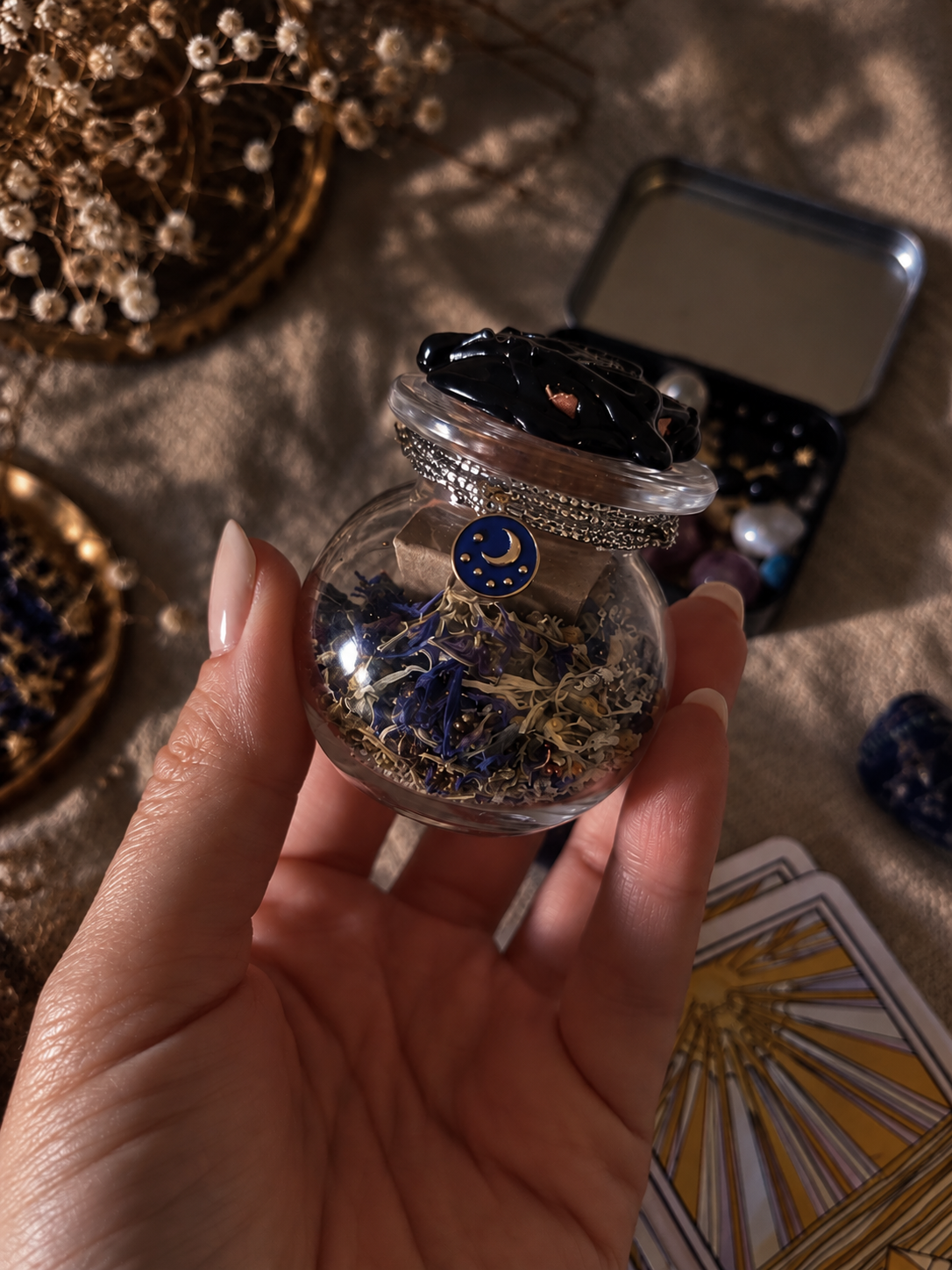 Petit bocal spell jar médiumnité tenu en main, rempli de fleurs bleues et blanches, cartes de tarot en arrière-plan
