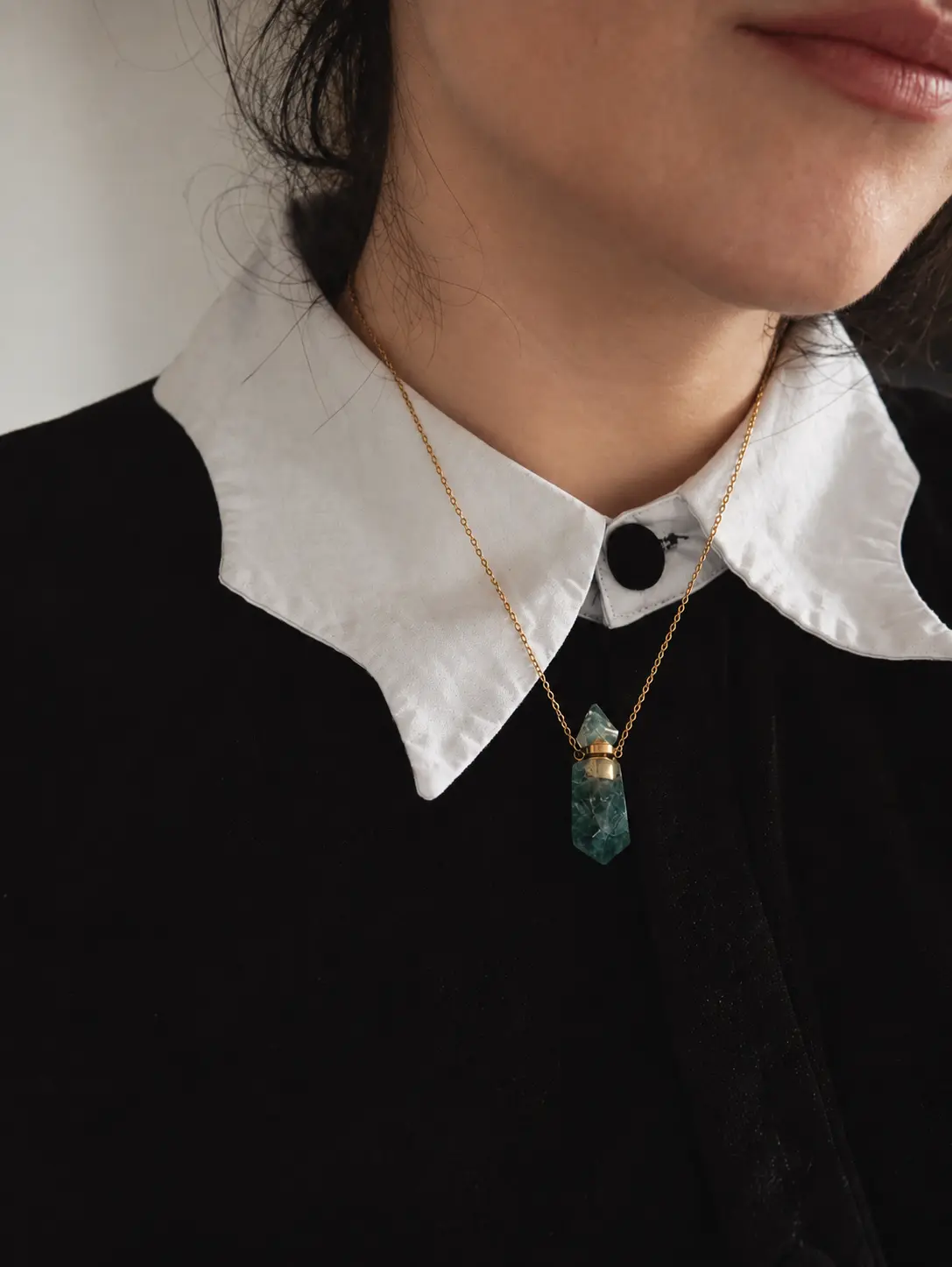 Collier amulette en aventurine verte porté sur un chemisier noir à col blanc